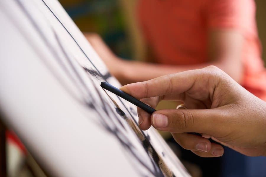 A person draws on a canvas with a charcoal stick.
