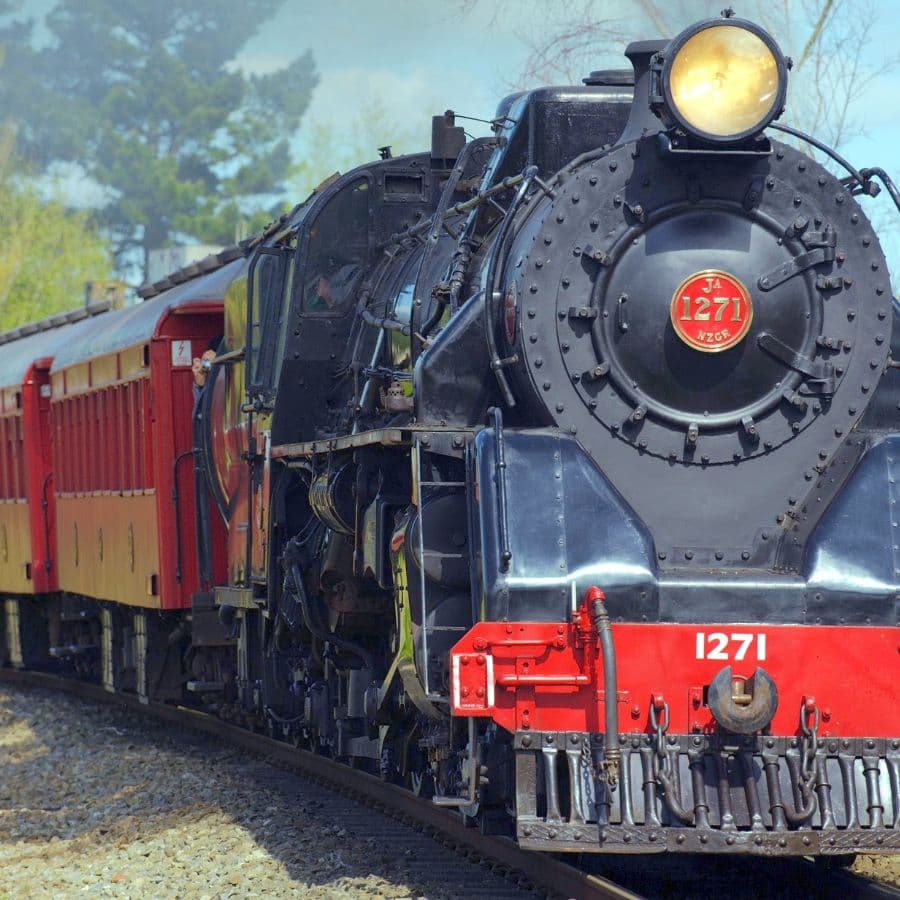 A vintage steam locomotive labeled "1271" pulls a set of colorful train cars along a track.