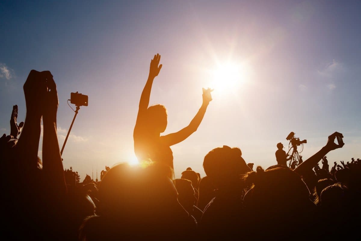 A silhouetted crowd raises their arms in celebration under a bright sun.