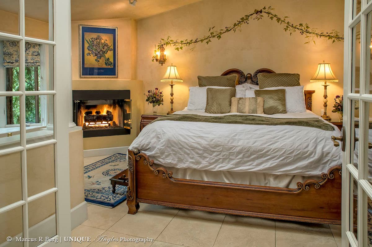 A cozy bedroom featuring a large bed, decorative pillows, and a warm fireplace.