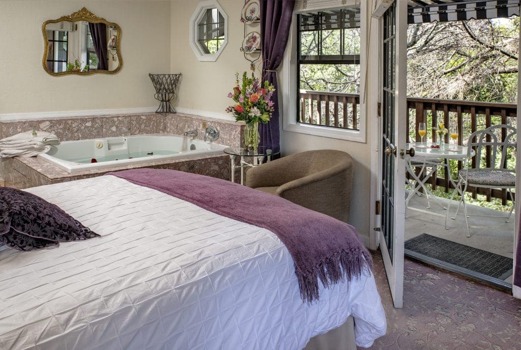 A cozy bedroom featuring a queen-sized bed, a jacuzzi, and a balcony with outdoor seating.