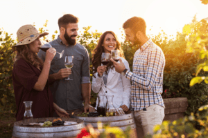 A group of four friends enjoys wine tasting outdoors at a vineyard during sunset. A group of four friends enjoys wine tasting outdoors at a vineyard during sunset.