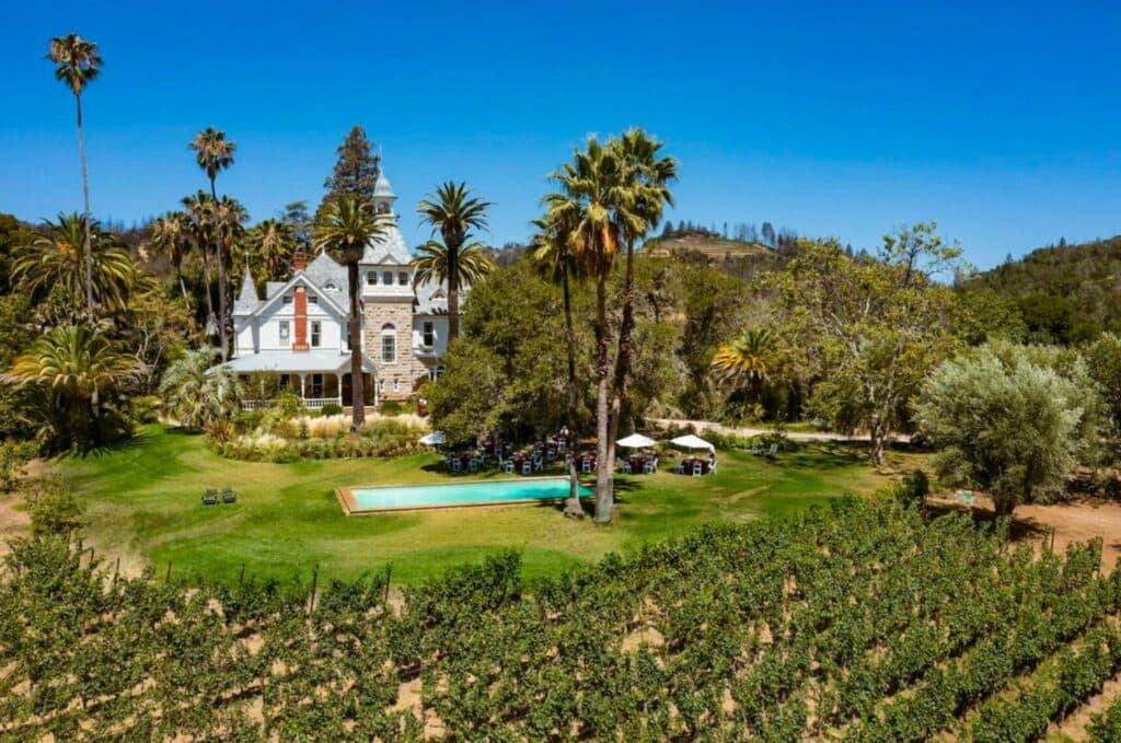 A scenic vineyard with a historic mansion surrounded by palm trees and a pool.