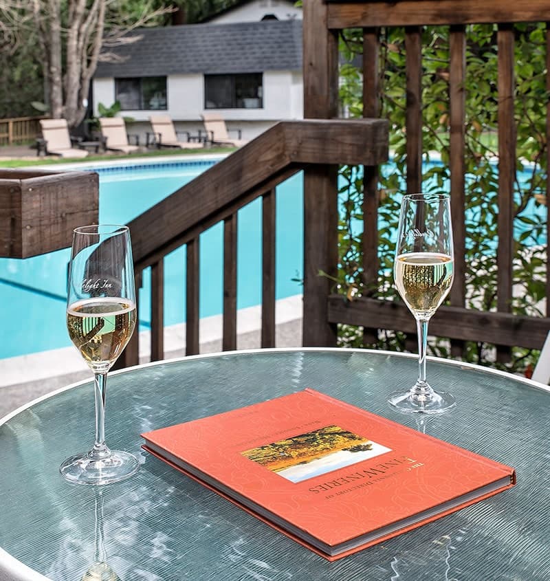 Two glasses of sparkling wine sit on a table next to a menu, with a pool and lounge chairs in the background.
