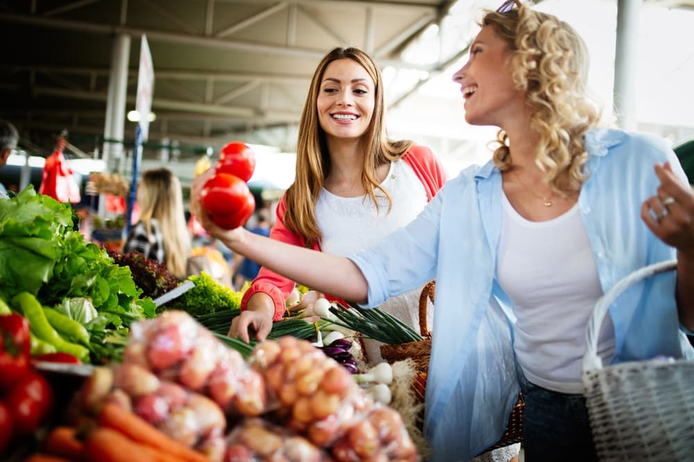 Two women happily shopping for fresh produce at a market.