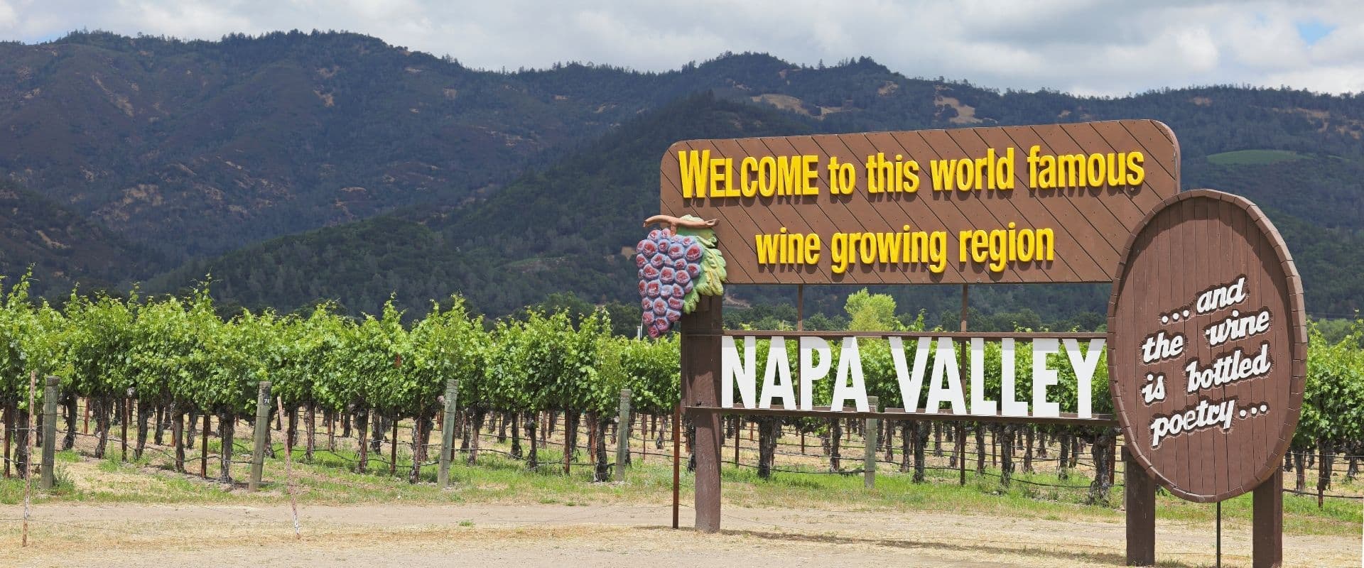 Sign welcoming visitors to Napa Valley, surrounded by vineyards and mountains.