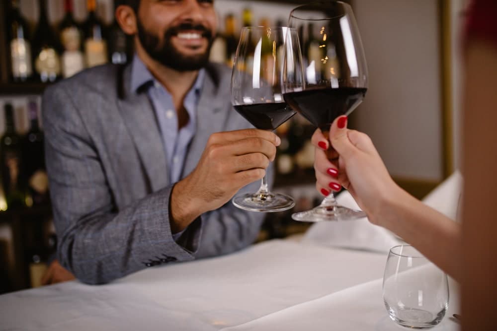 Two people clinking glasses of red wine at a restaurant.