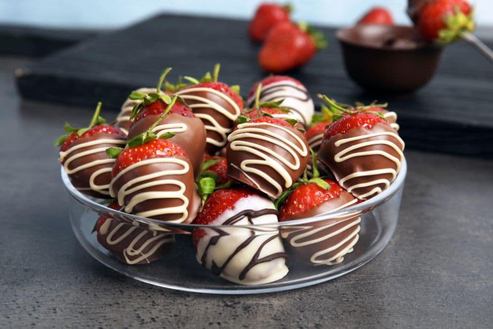 A clear glass bowl filled with chocolate-covered strawberries drizzled with white chocolate.