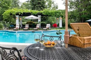 A beautifully set outdoor table by a swimming pool, featuring a wine glass, a bowl of fruit, and a picnic basket with a rose in a vase. A beautifully set outdoor table by a swimming pool, featuring a wine glass, a bowl of fruit, and a picnic basket with a rose in a vase.