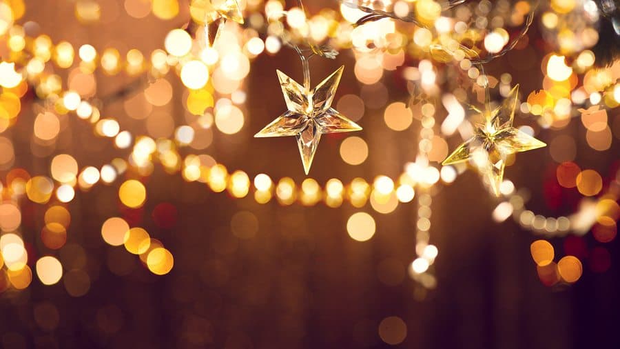 Glistening star-shaped ornaments hang amid a backdrop of warm, blurred lights.