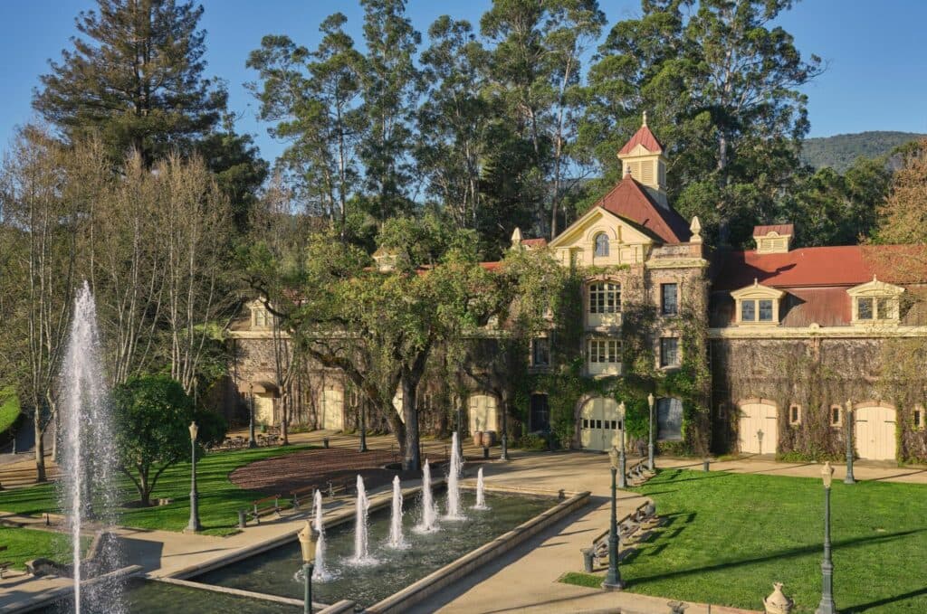 A historic building surrounded by trees and a fountain in a landscaped garden.