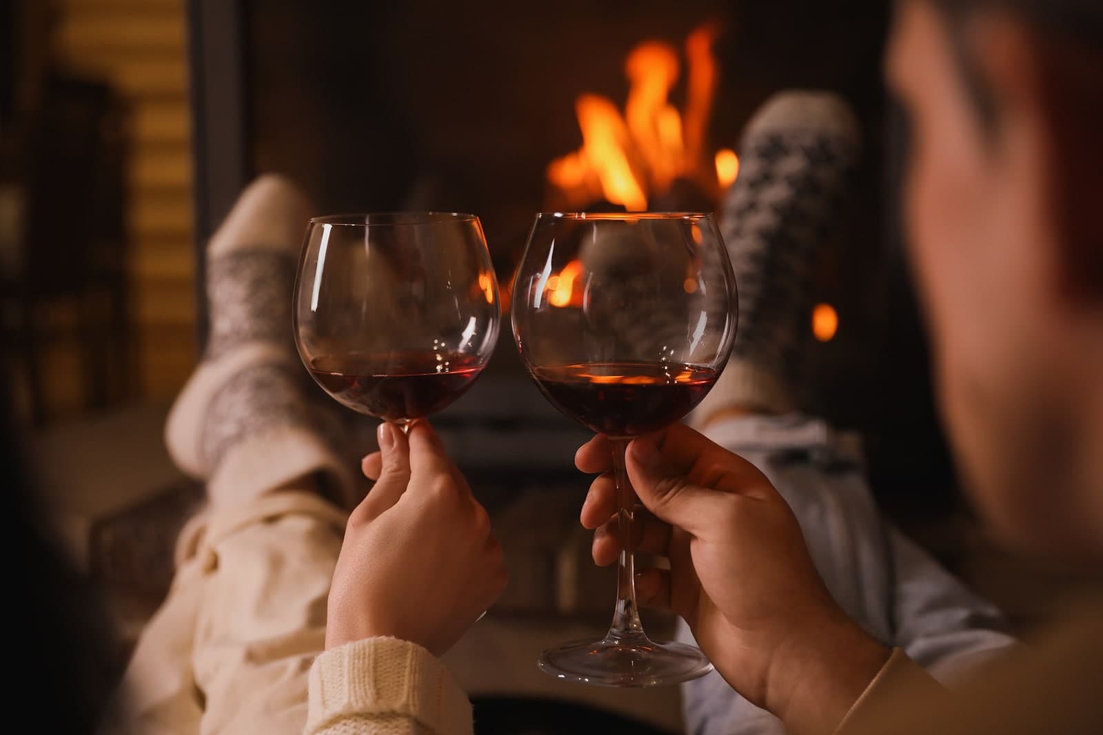 Two hands holding wine glasses in front of a cozy fire. Two hands holding wine glasses in front of a cozy fire.