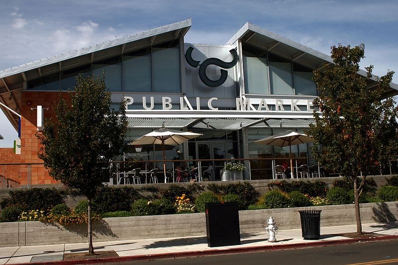 A modern market building with a large "Public Market" sign and outdoor seating under umbrellas.